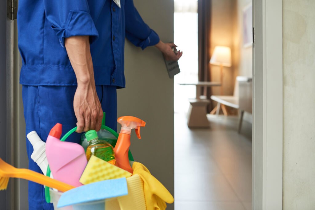 Professional cleaner with bucket of detergents opening room